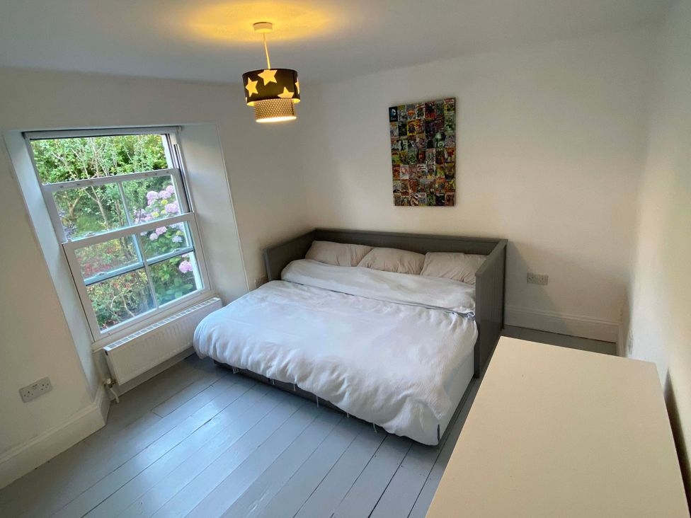 A bedroom with a bed and window at Strand House Treknow near Tintagel