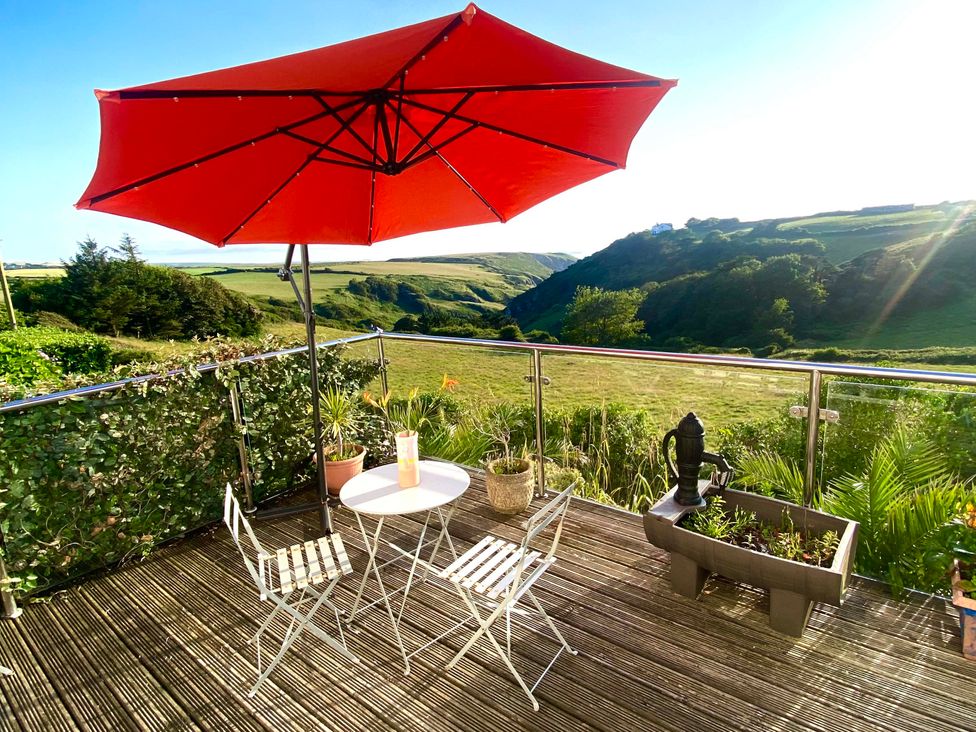 An outdoor patio with chairs and a table under a red parasol at Strand House in Treknow near Tintagel