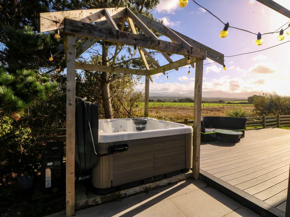 A hot tub under a wooden pergola in the garden at Cae Mawr Dinas Dinlle