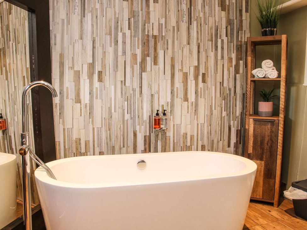A bathroom with a bathtub and shelves holding towels at The Half Boar in Bishop's Castle