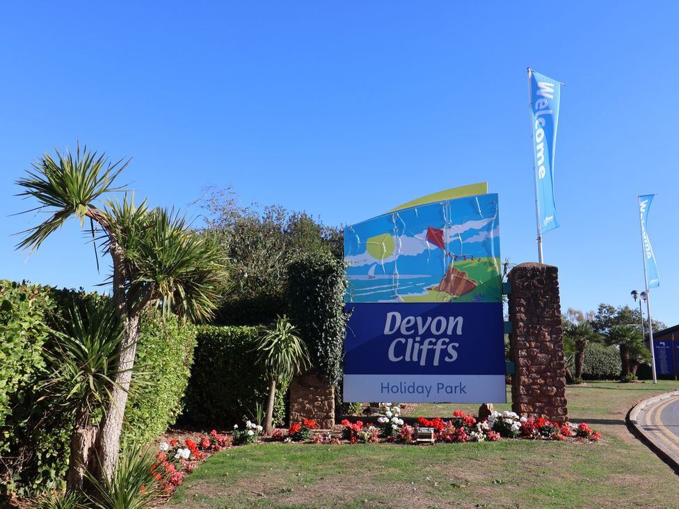 A sign for Devon Cliffs Holiday Park with plants and flowers in Sandy Bay, Exmouth