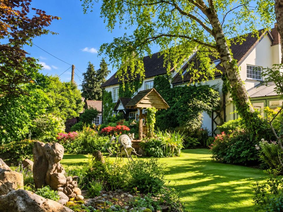 A garden with a house, trees, flower beds, and a fountain at Holdfast Cottage Sleeps 12 in The New Forest, Bramshaw near Totton, Hampshire