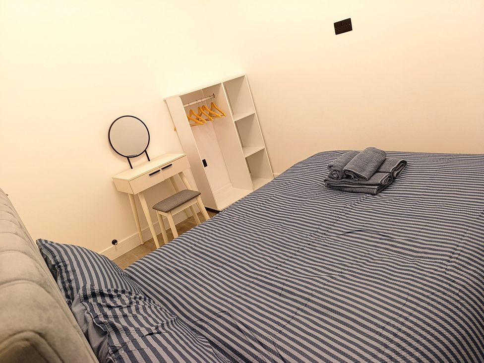 A bedroom with a bed, towels, mirror, desk, and wardrobe at Cardiff Cozy One Bedroom Apartment in Cardiff