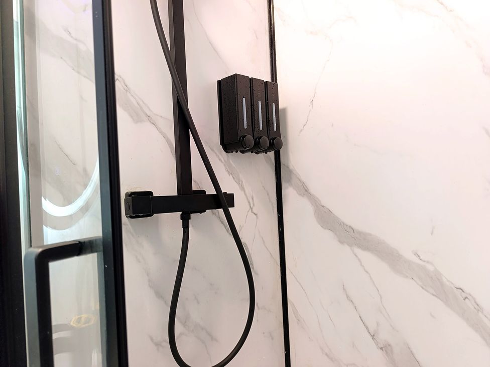 A shower setup with a showerhead and caddy in a marble bathroom at Cardiff Cozy One Bedroom Apartment in Cardiff