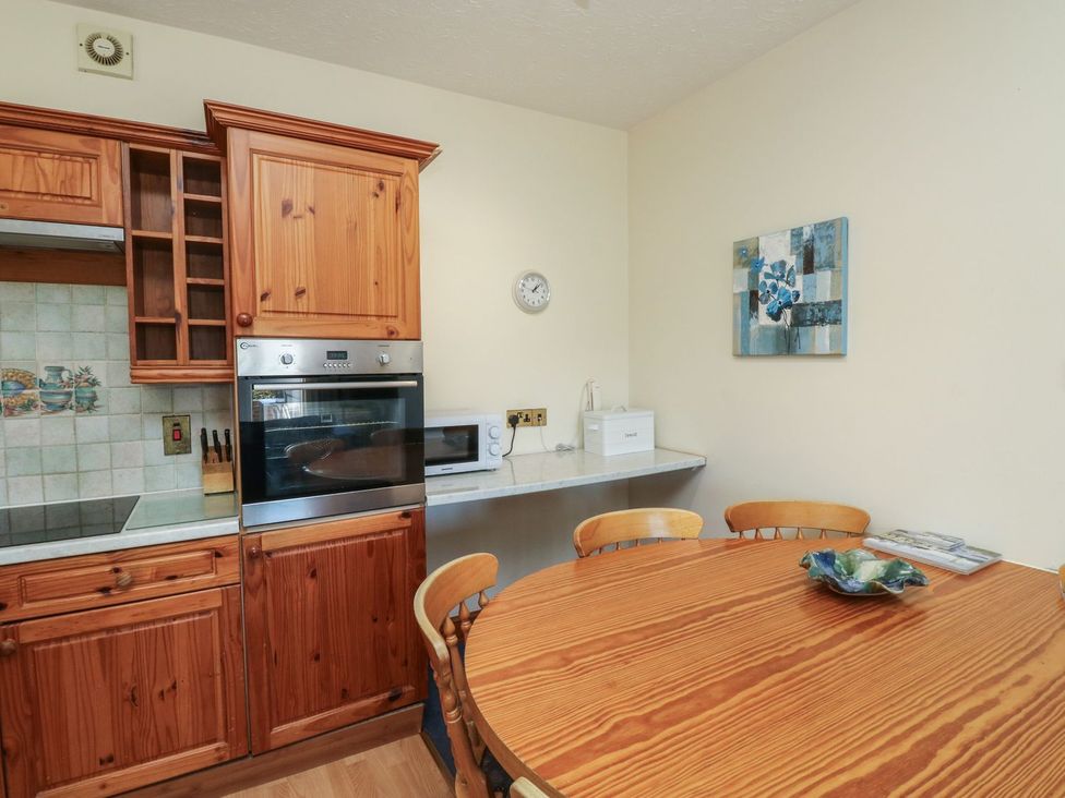 A kitchen with wooden cabinets and a round table at Avocet in Kingsteignton