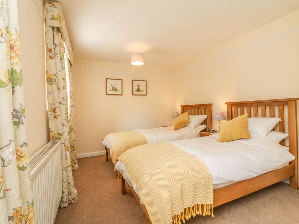 A bedroom with two beds and floral curtains at Upper Barn Cottage Minehead
