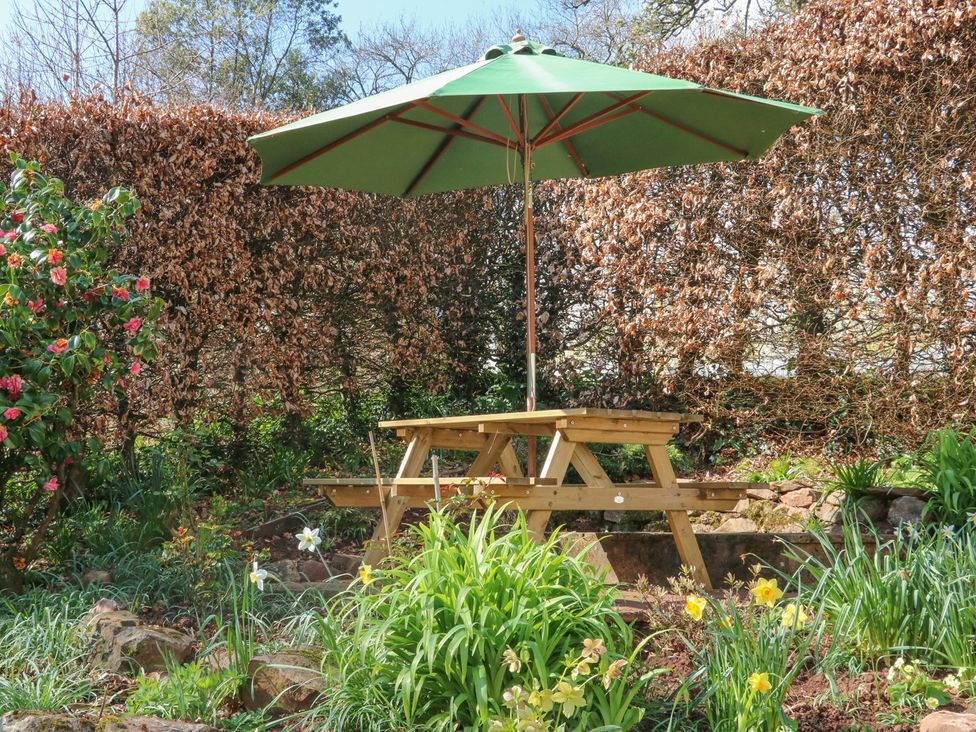 A table with benches and an umbrella in a garden at Upper Barn Cottage Minehead