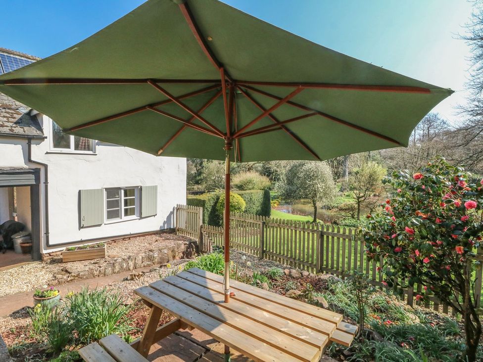 A garden with a wooden table and an umbrella at Upper Barn Cottage Minehead