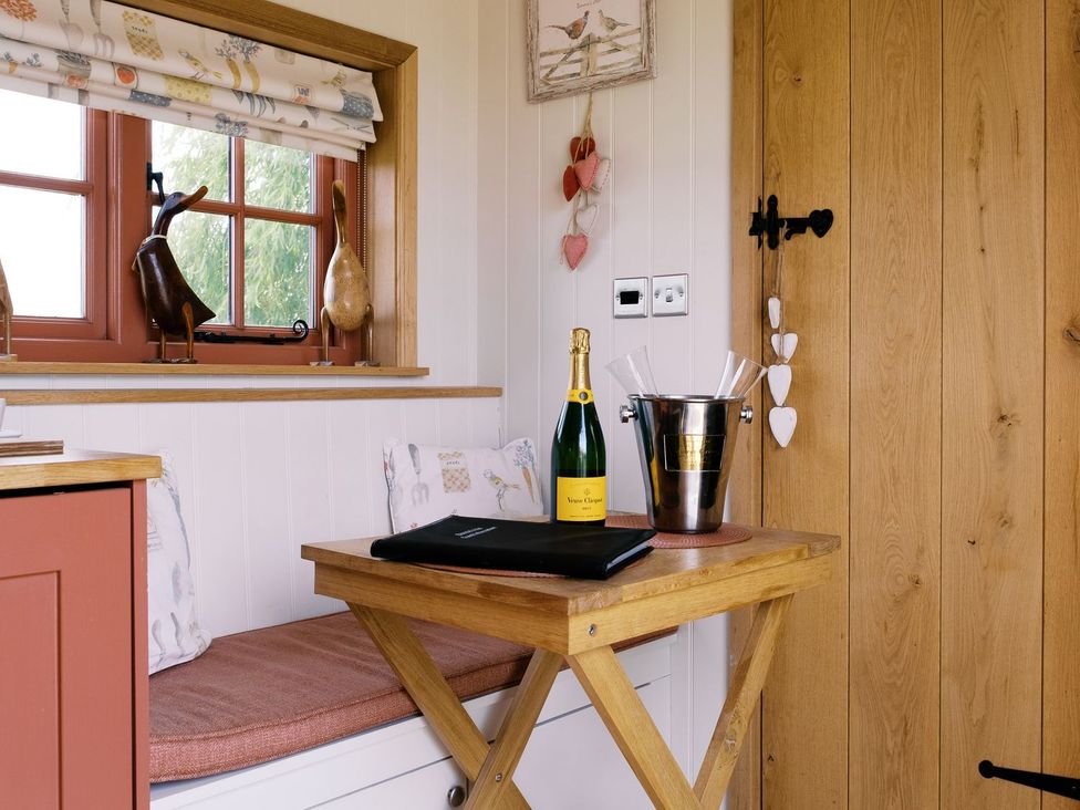 A snug area with a window, table, and champagne at Bonnie's Shepherds Hut at Shepherds Lodge Retreat and Wellness Nottingham