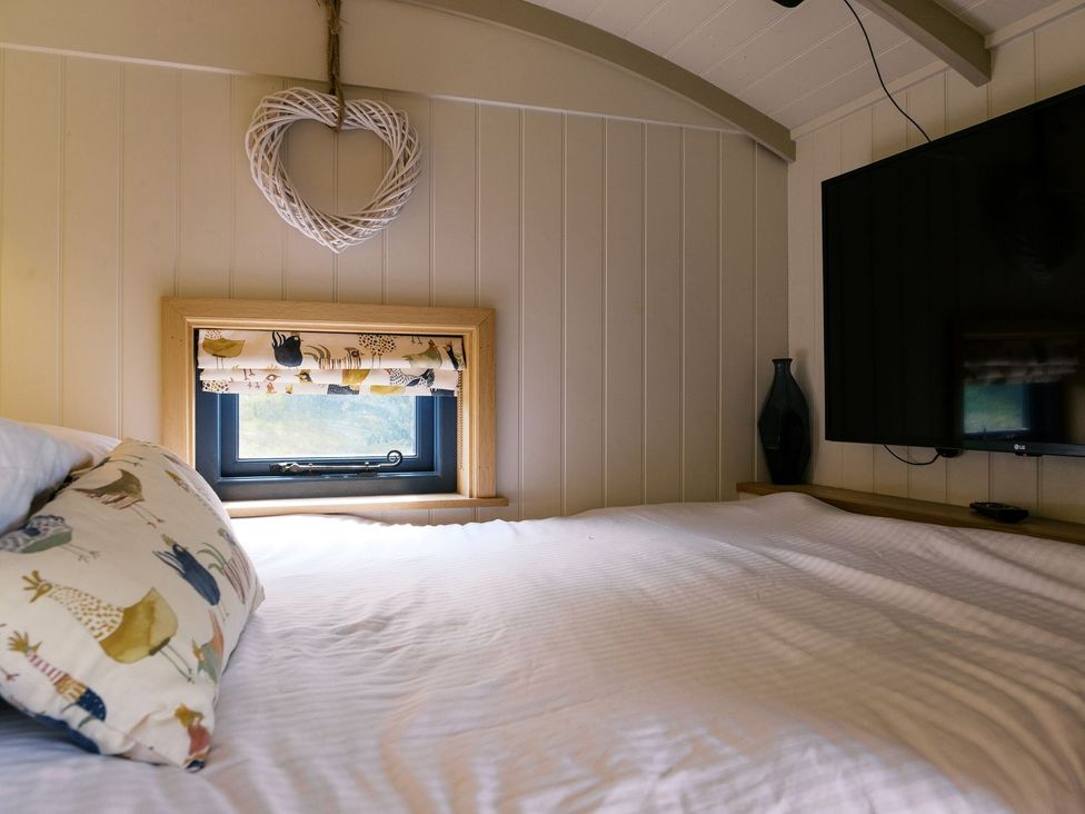 A bedroom featuring a bed, decorative pillow, window with curtain and TV at Lillie's Shepherds Hut at Shepherds Lodge Retreat and Wellness, Nottingham