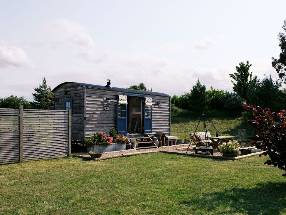 A wooden hut with outdoor seating and a table at Lillie's Shepherds Hut at Shepherds Lodge Retreat and Wellness Nottingham