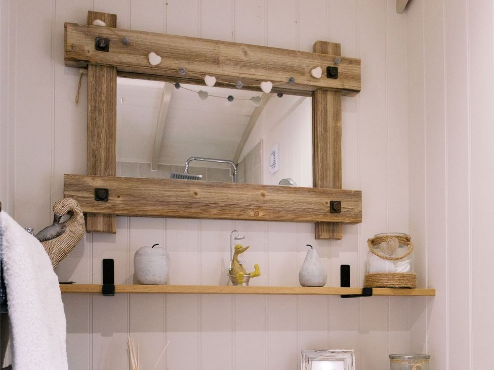 A bathroom with a mirror and shelf displaying decorative items at Herbie's Shepherds Hut at Shepherds Lodge Retreat and Wellness Nottingham