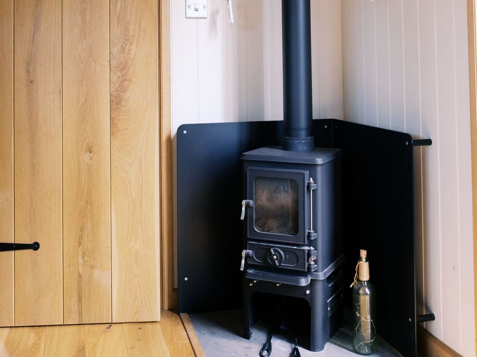 A wood stove in a corner with a bottle at Poppie's Shepherds Hut at Shepherds Lodge Retreat and Wellness Nottingham