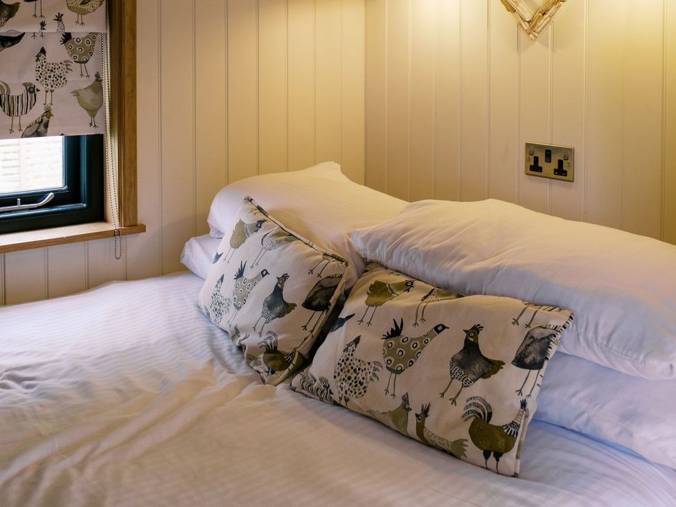 A bed with patterned pillows and a window at Poppie's Shepherds Hut at Shepherds Lodge Retreat and Wellness Nottingham