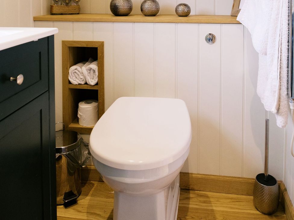 A bathroom with a toilet and shelf storing towels at Poppie's Shepherds Hut at Shepherds Lodge Retreat and Wellness Nottingham