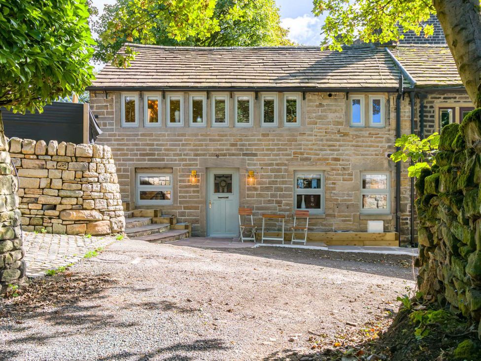 An exterior view of a stone house with a gravel driveway and outdoor seating at Heaven Lea Cottage