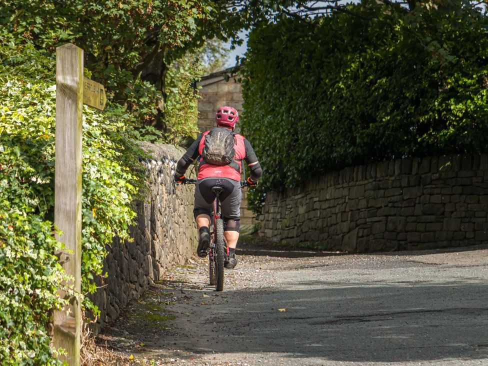 A cyclist riding on a path beside a stone wall and signpost at Heaven Lea Cottage