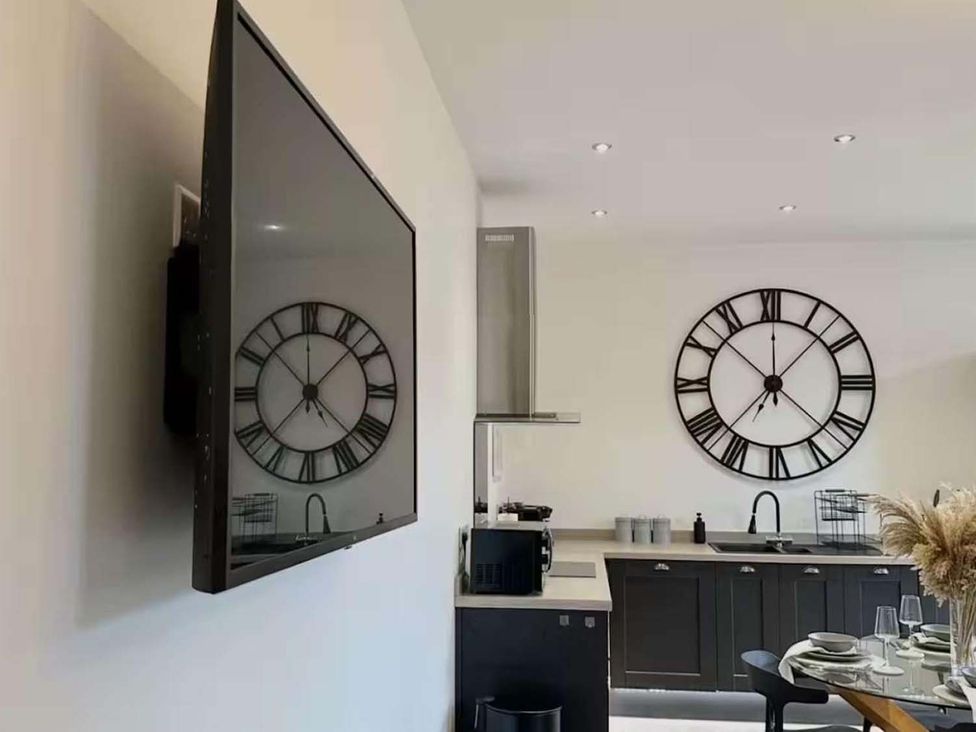 A kitchen with a television and wall clock at New Cosy Retreat in Matlock Bath