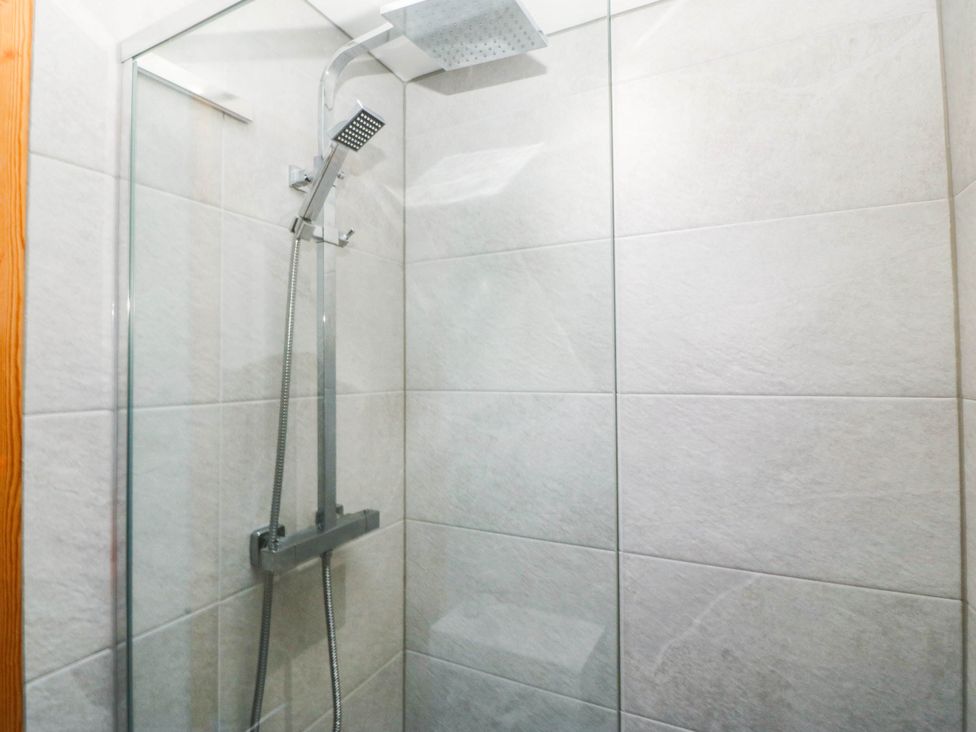 A shower with a glass panel and tiles at Derwen-Las in Penmaenmawr