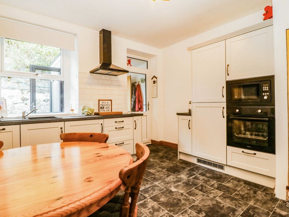 A kitchen with a round wooden table and appliances at Derwen-Las in Penmaenmawr