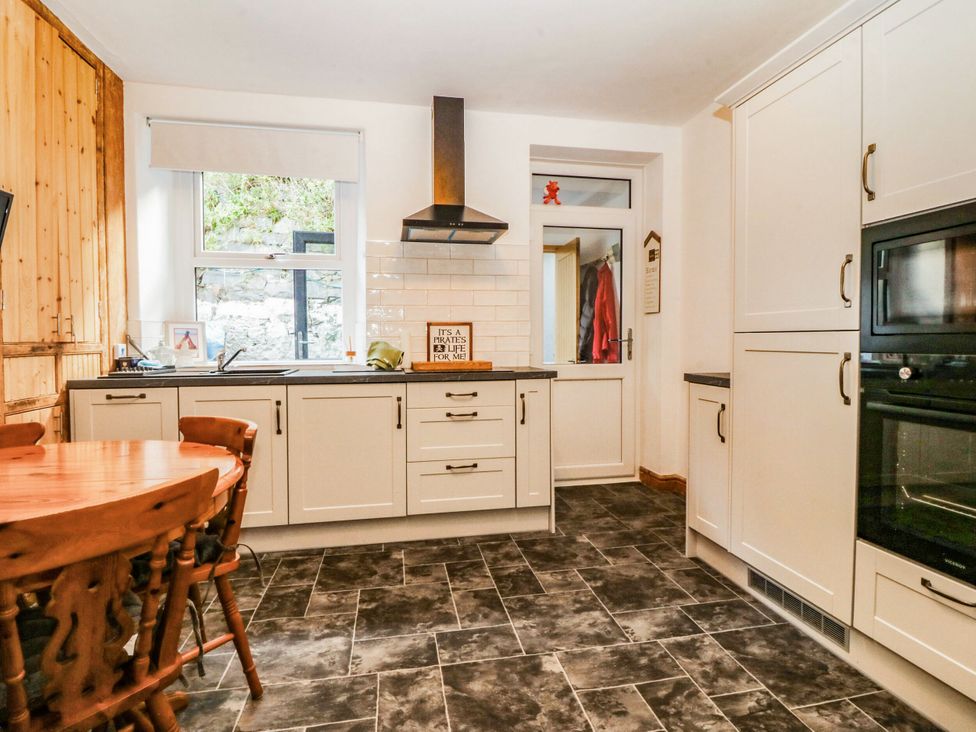 A kitchen with cabinets, a table, and a sink at Derwen-Las in Penmaenmawr