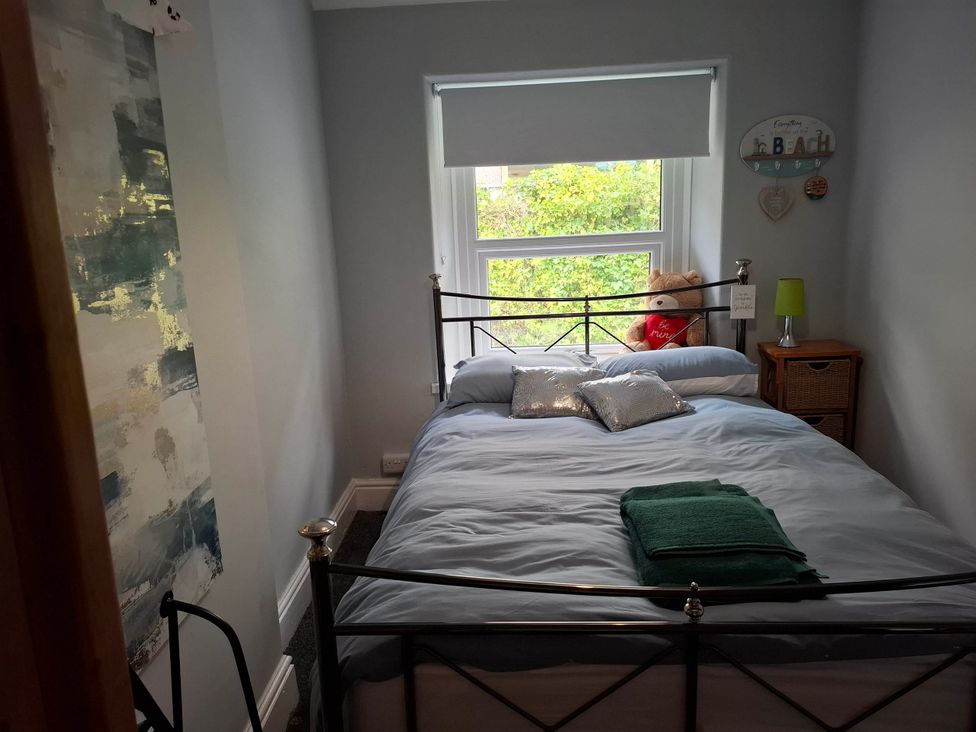 A bedroom with a metal bed and window view at Derwen-Las in Penmaenmawr
