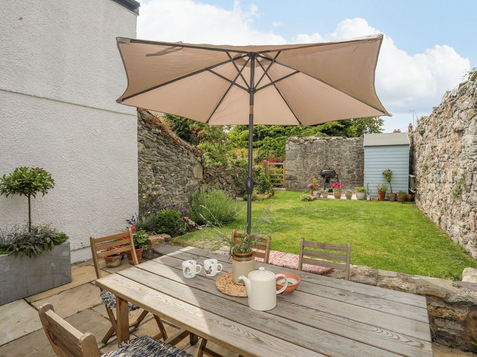 A garden with a table and chairs under an umbrella at Swn y Mor (Wexham) Beaumaris