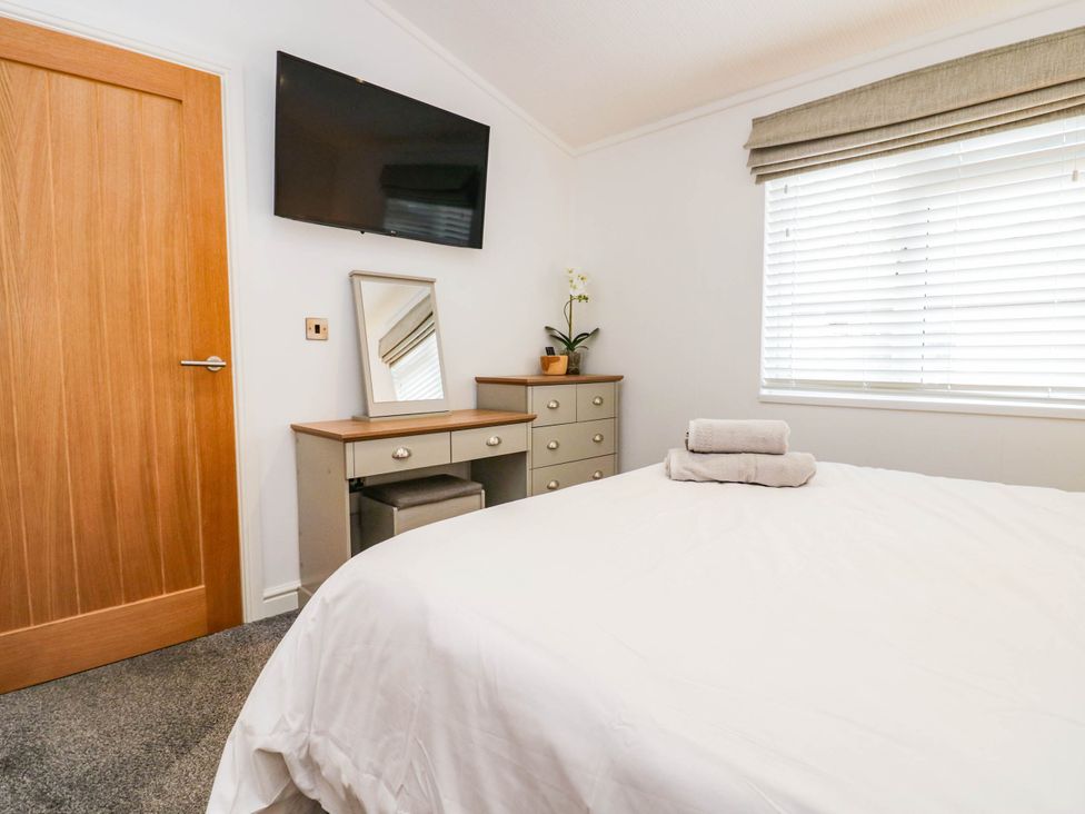 A bedroom featuring a bed, dresser, mirror, and television at Thirlmere Scar in Windermere