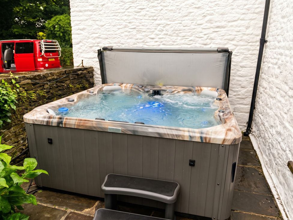 A hot tub with steps next to a stone wall at Tynewydd Farmhouse