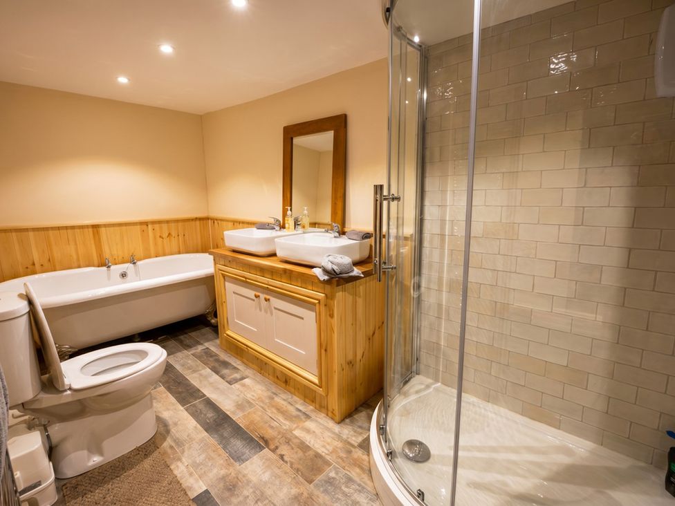 A bathroom with a bathtub, a toilet, sinks, and a shower at Tynewydd Farmhouse