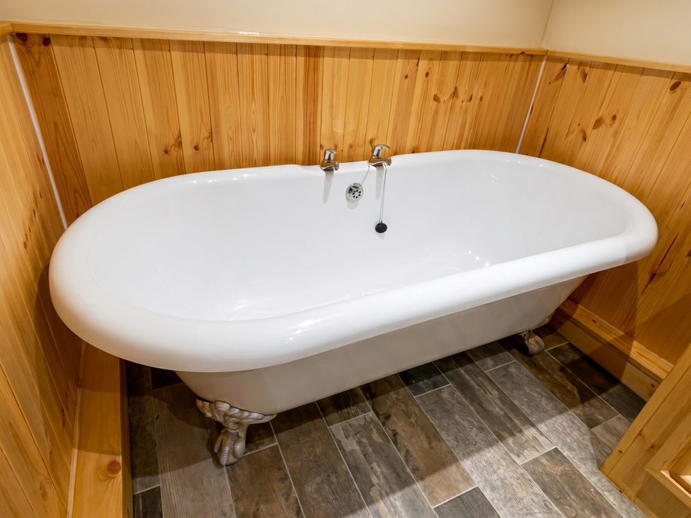 A bathroom with a white bathtub and wooden paneling at Tynewydd Farmhouse