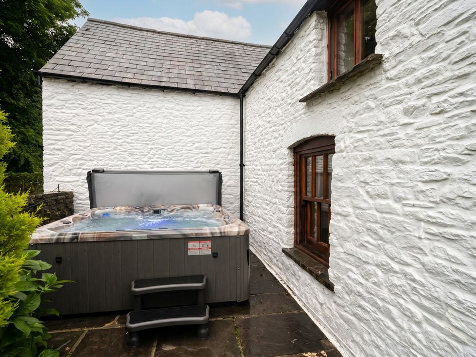 A hot tub with steps outside a white stone house at Tynewydd Farmhouse