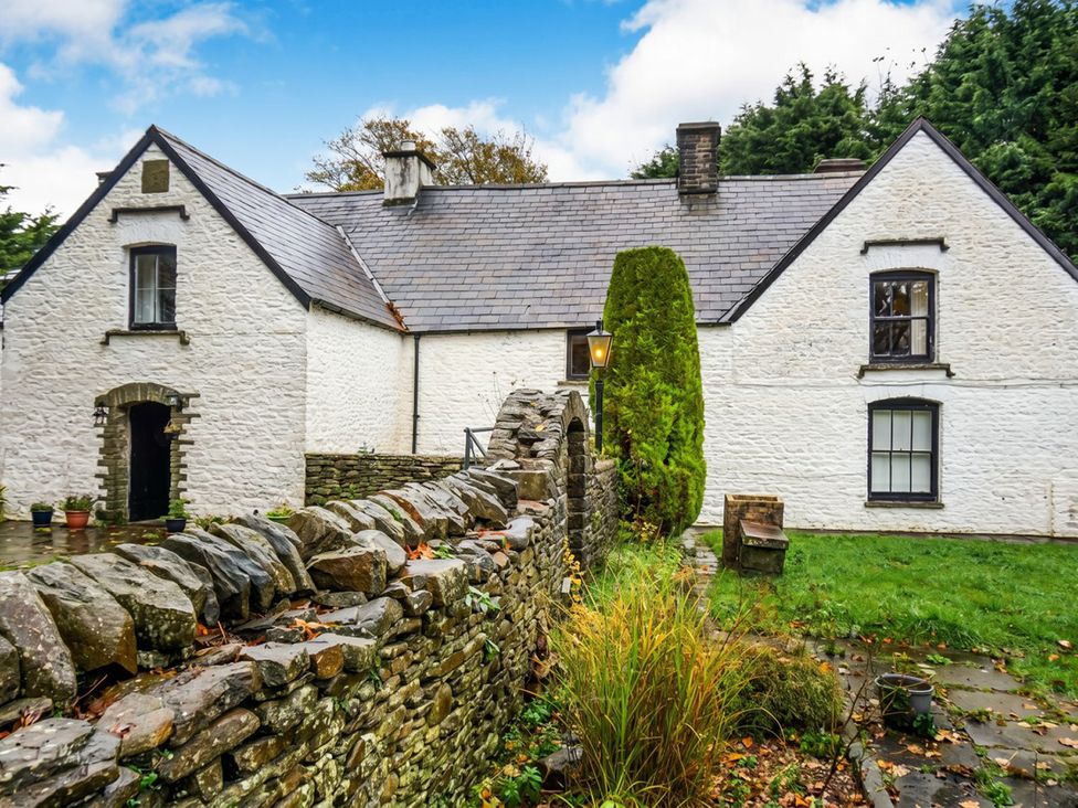 An outdoor view of a house with a garden and stone wall at Tynewydd Farmhouse