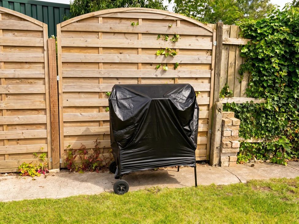 A covered grill next to a wooden fence in a garden