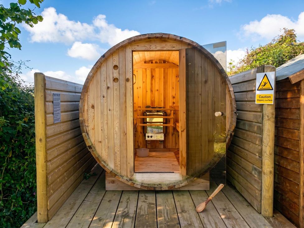 A wooden barrel sauna with an open door and a bench inside at outdoor location