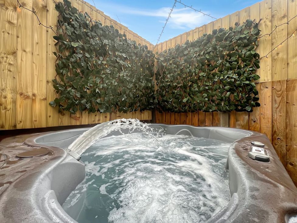 A hot tub with water jets in an outdoor area surrounded by wooden panels and greenery