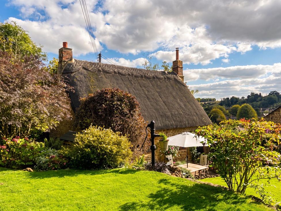 An outdoor area with a thatched roof cottage, garden furniture and plants