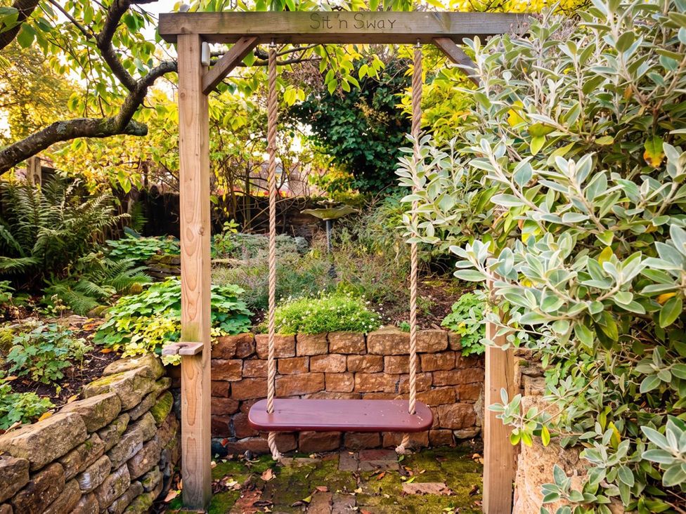 A swing in a garden surrounded by plants and a stone wall at 