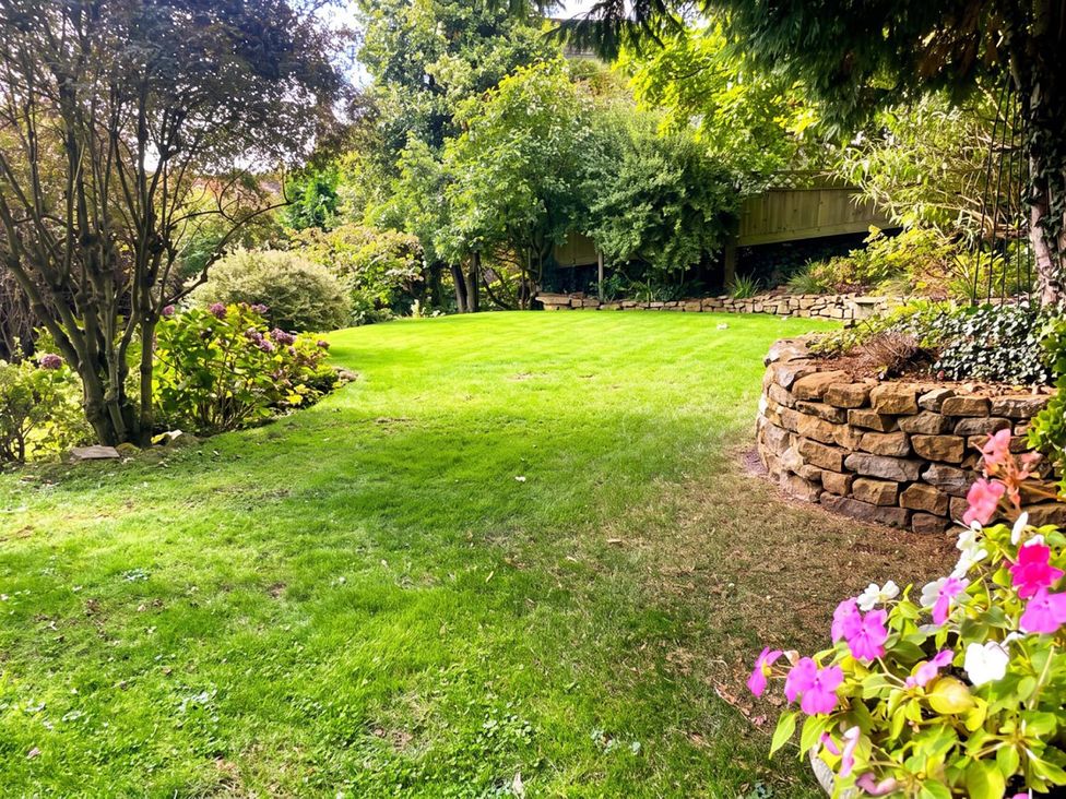 A garden with grass, flowers, trees, and a stone wall at 