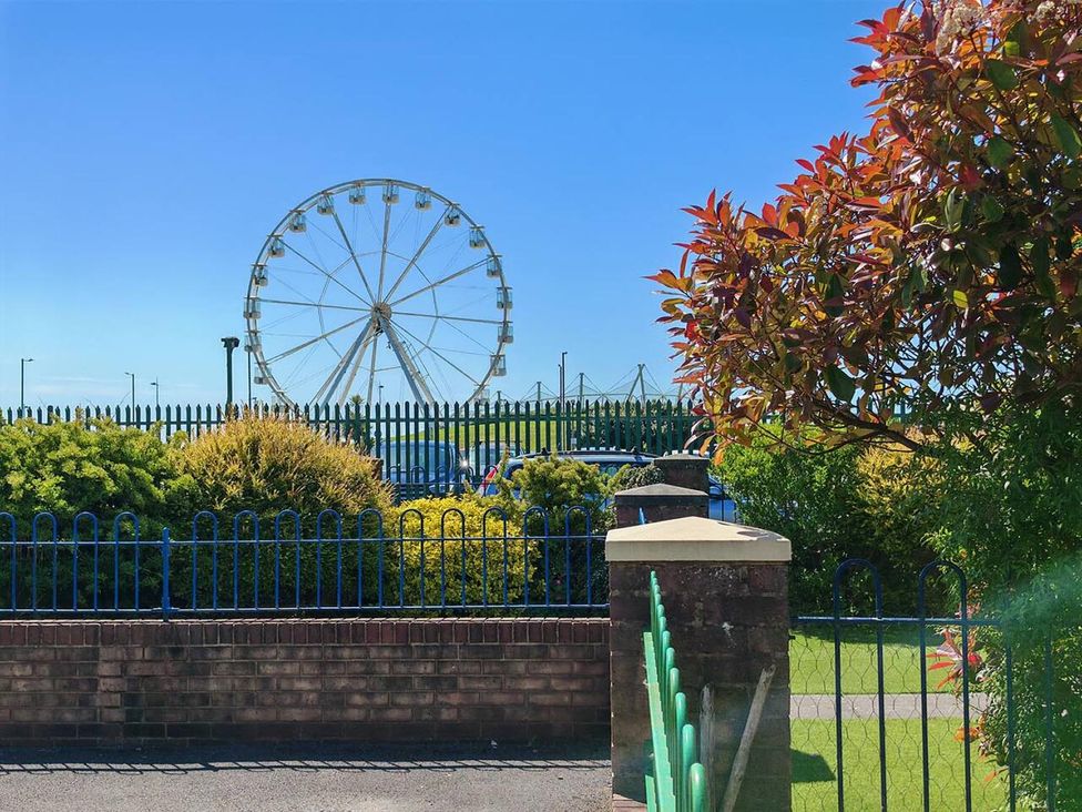 A ferris wheel seen through a fence with bushes at a park