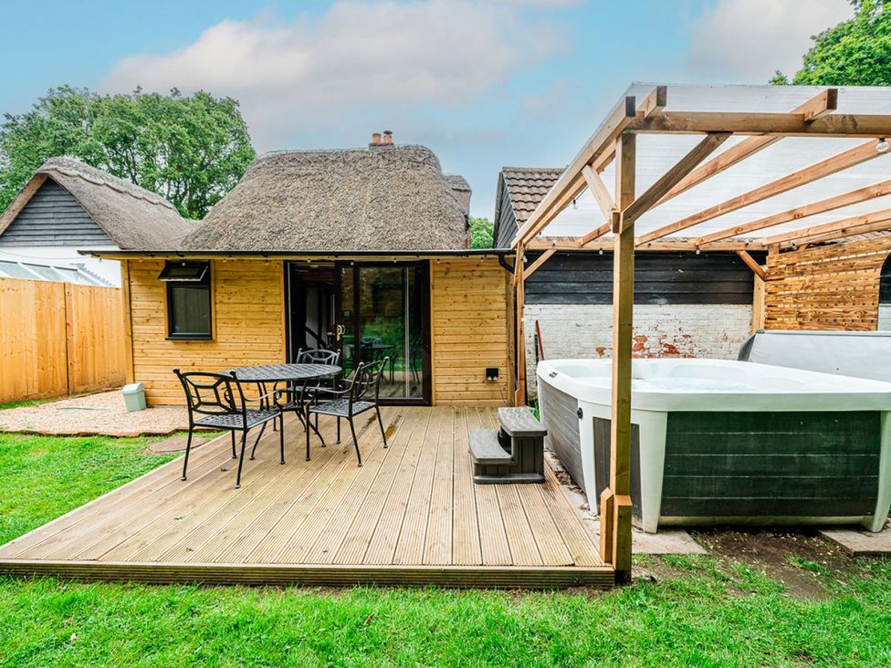 A garden with a wooden deck, table, chairs, and hot tub at a property