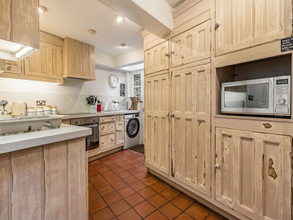 A kitchen with cabinets, microwave, oven and washing machine at Quay Cottage