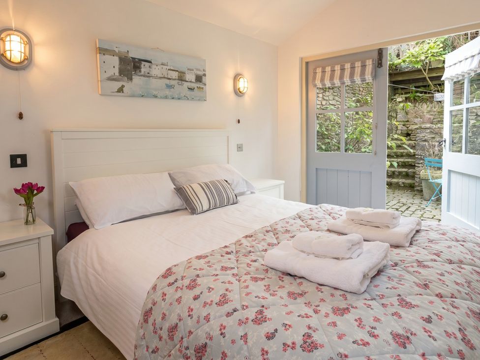 A bedroom with a bed and an open door leading to an outdoor area at Quay Cottage