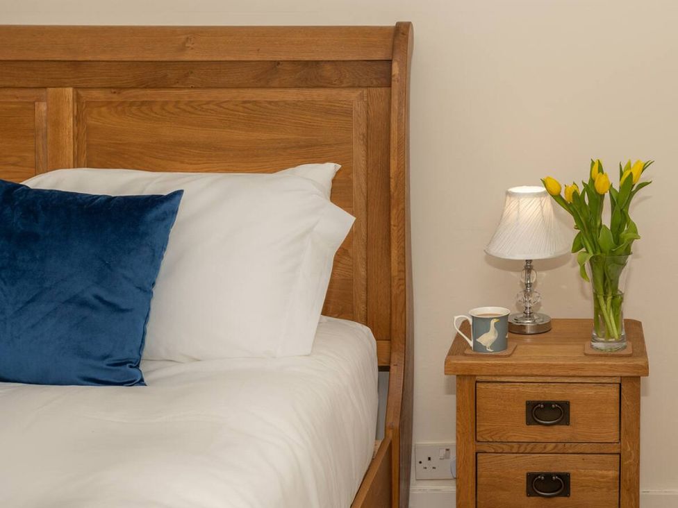 A bedroom with a wooden bed, nightstand, lamp, flowers, and a cup