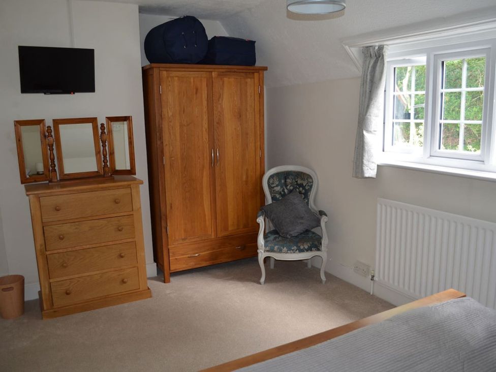 A bedroom with a wardrobe, dresser, armchair, and television