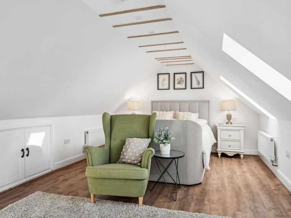A bedroom with armchair, bed, nightstand and lamp