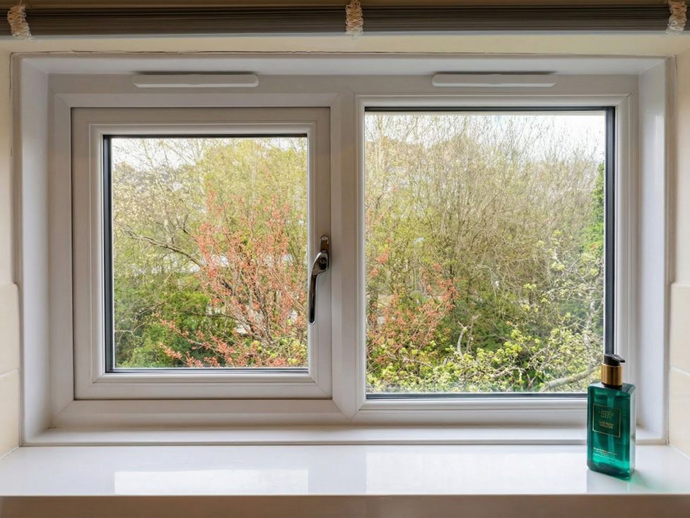 A window with a view of trees and a green bottle on the sill at the property in the location