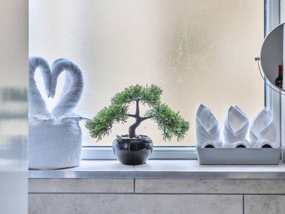 A bonsai tree and towel swans on a window sill in a bathroom