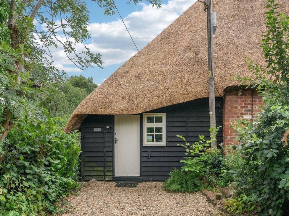 A thatched cottage with a door and window surrounded by greenery at Old Post Office