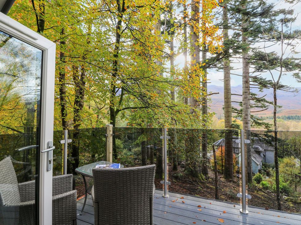 An outdoor balcony with table and chairs overlooking trees at Elleric Pods - The Last Resort Appin